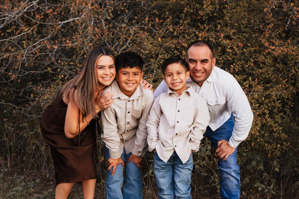A happy family poses together outdoors during a casual photo session against a natural backdrop.