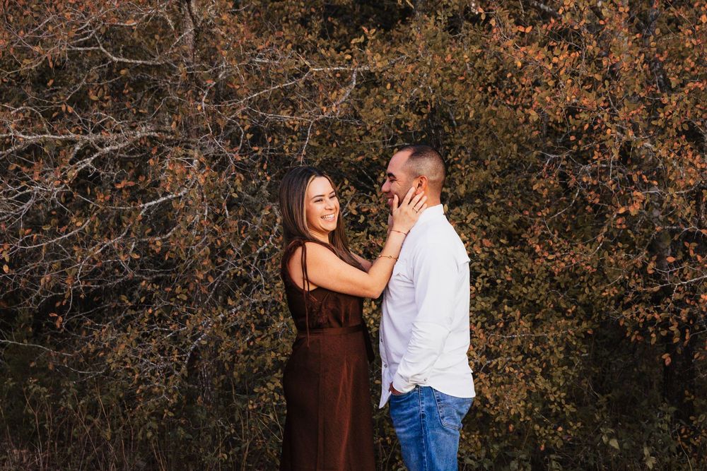 Couple embraces during autumn photoshoot with rustic orange foliage in background.