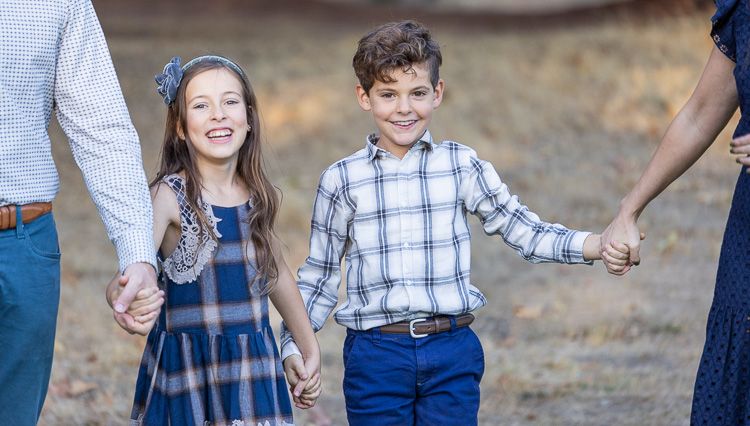 A family holds hands while walking outdoors in coordinated blue and white plaid outfits.