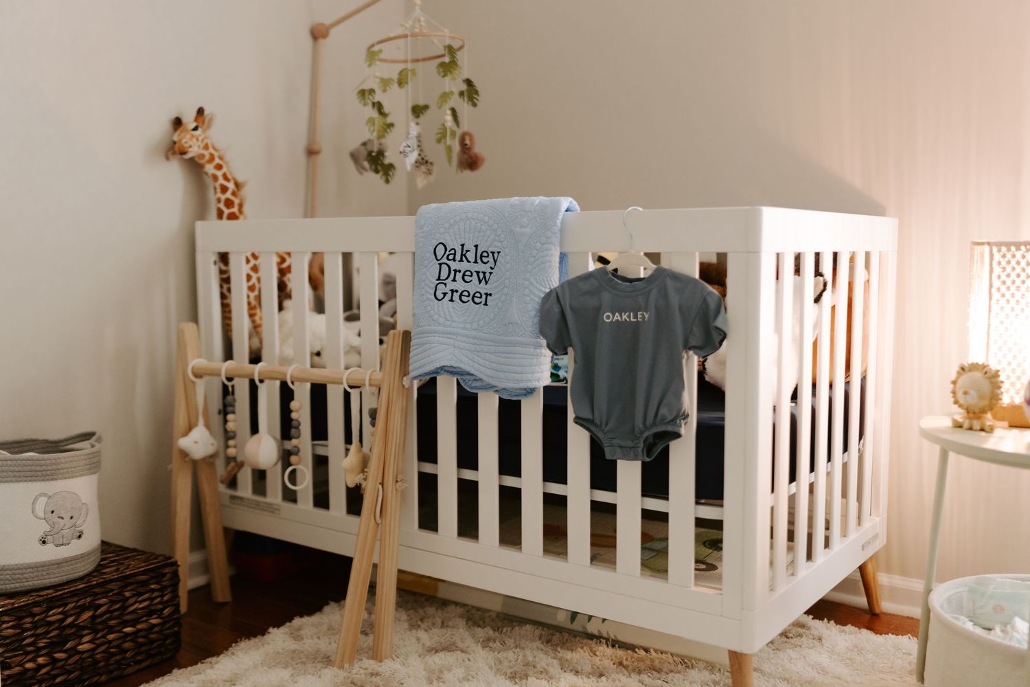 Modern white crib with wooden accents and hanging mobile in a minimalist nursery.