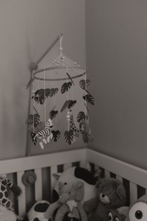 Black and white photo of nursery crib with hanging mobile and stuffed animals.
