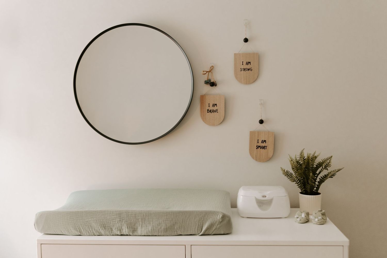 Minimalist white nursery decor with floating shelves and a round mirror.
