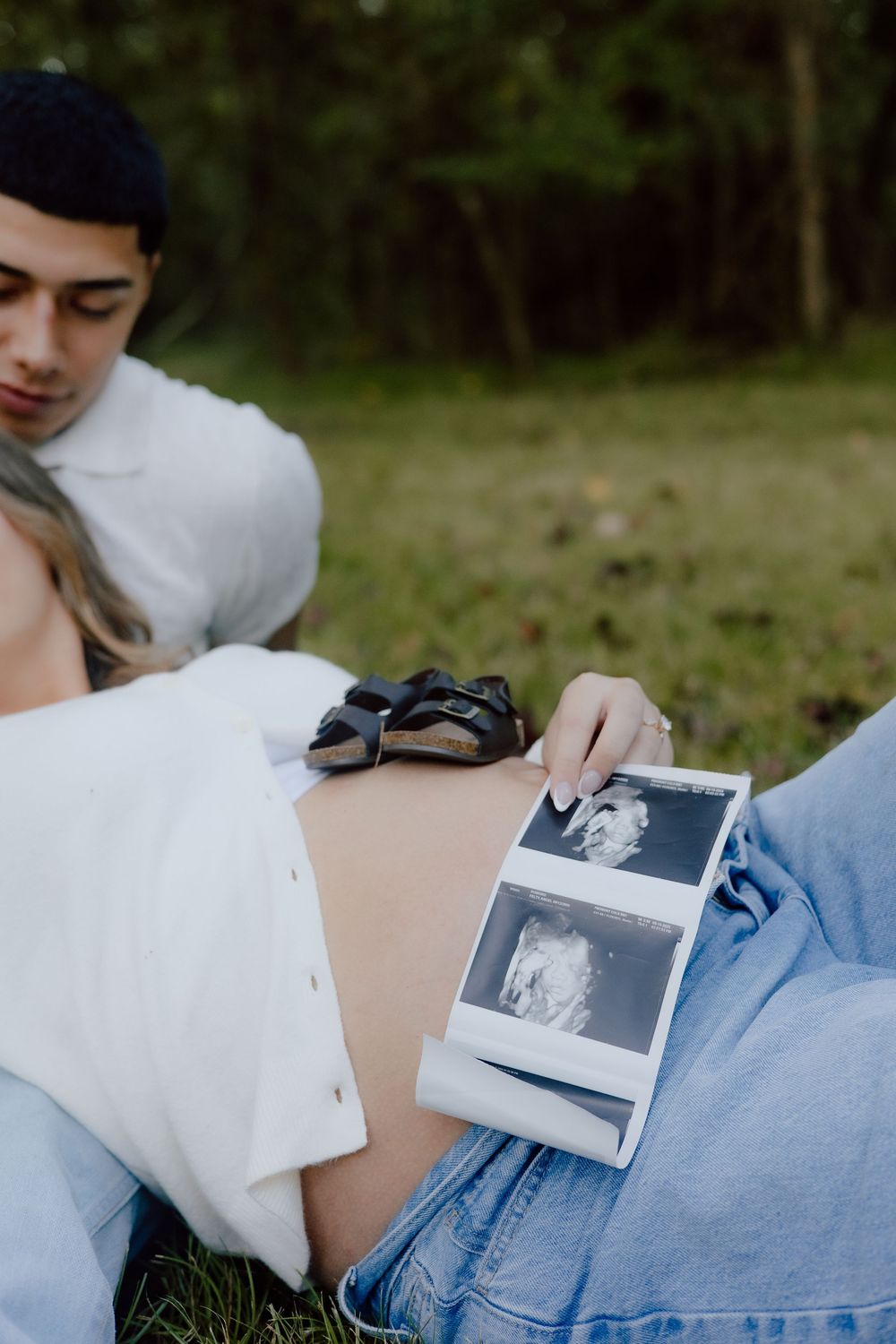 A couple looks at black and white polaroid photos together while sitting outdoors.