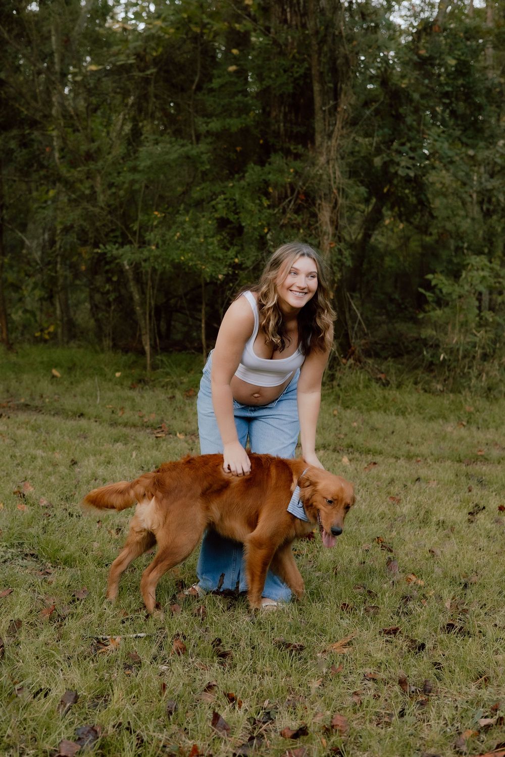 A person in blue jeans and tank top plays with a happy golden retriever dog on grassy field.
