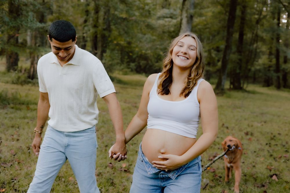 Couple holds hands and walks together through a wooded area on a sunny afternoon.