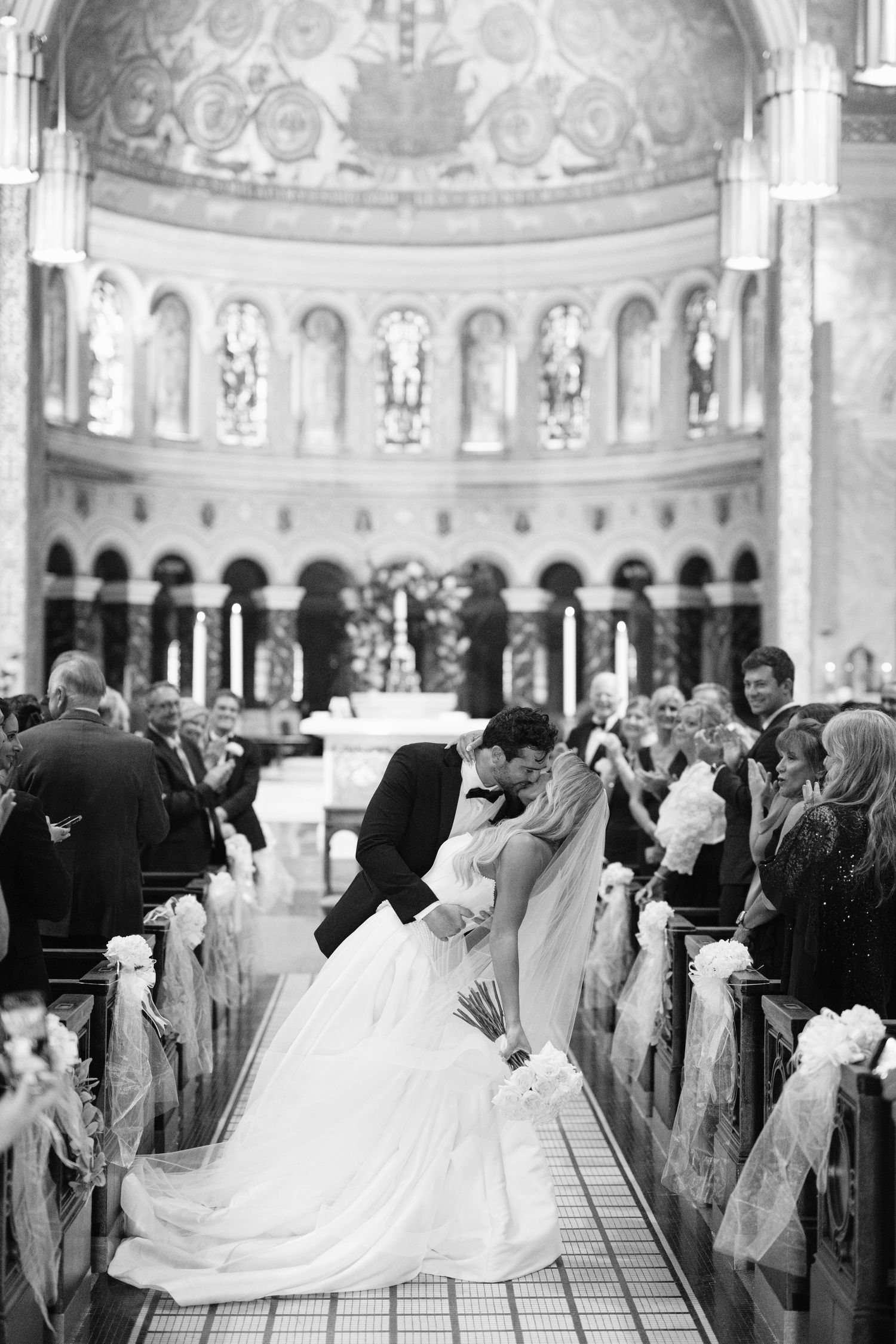 A black and white photograph shows a wedding ceremony taking place inside an ornate cathedral with a domed ceiling.