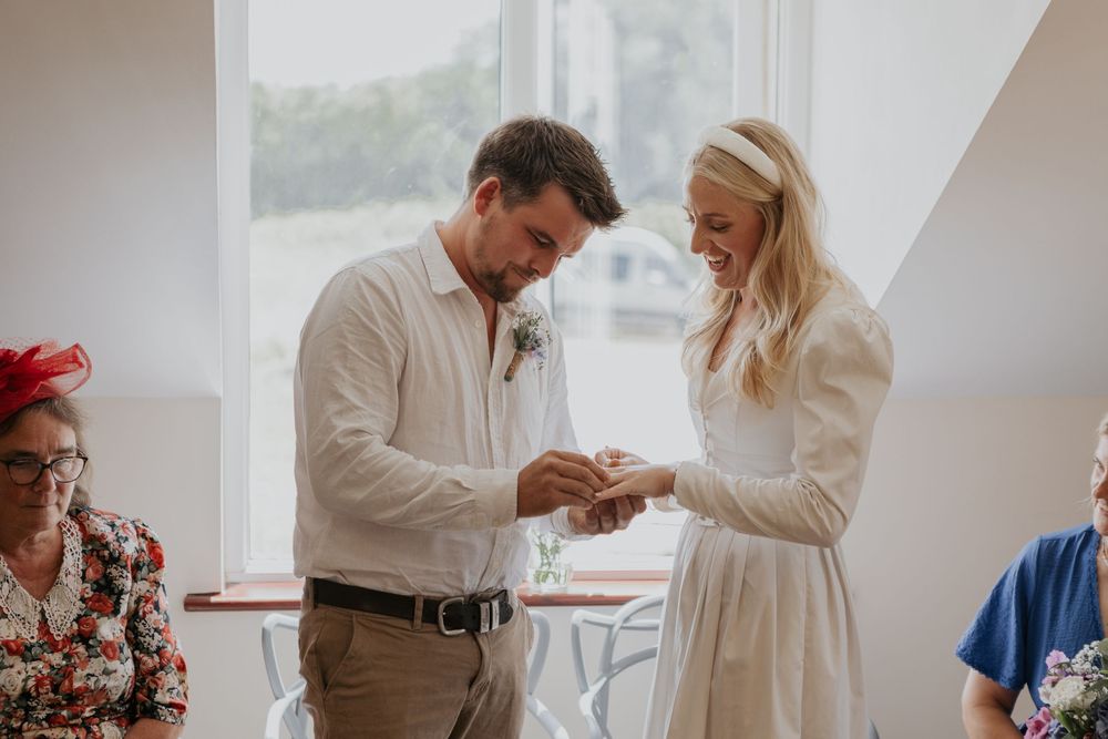 Smiling bride places wedding ring on grooms finger during joyful intimate wedding ceremony.