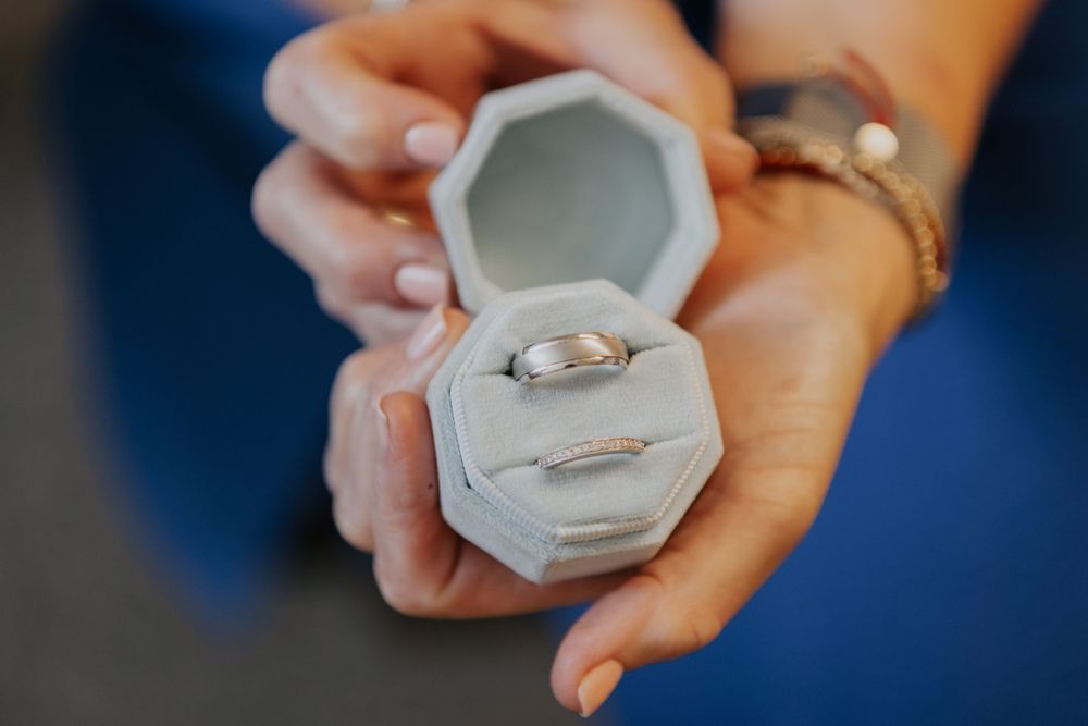 Two silver wedding bands displayed in an open gray velvet octagonal ring box held by hands.