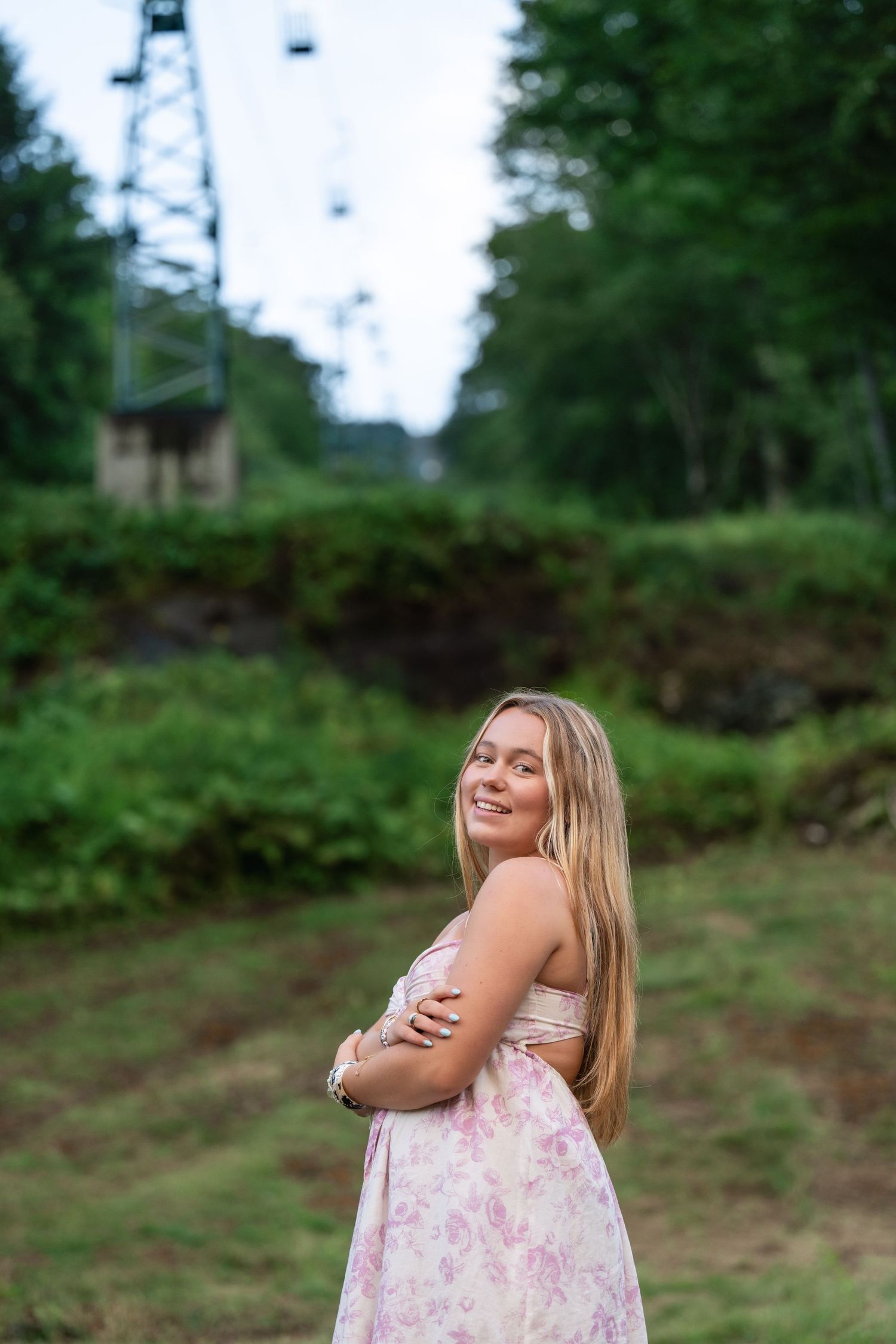 A person in a pink floral dress stands in a garden with blooming azaleas and ferns in the background.