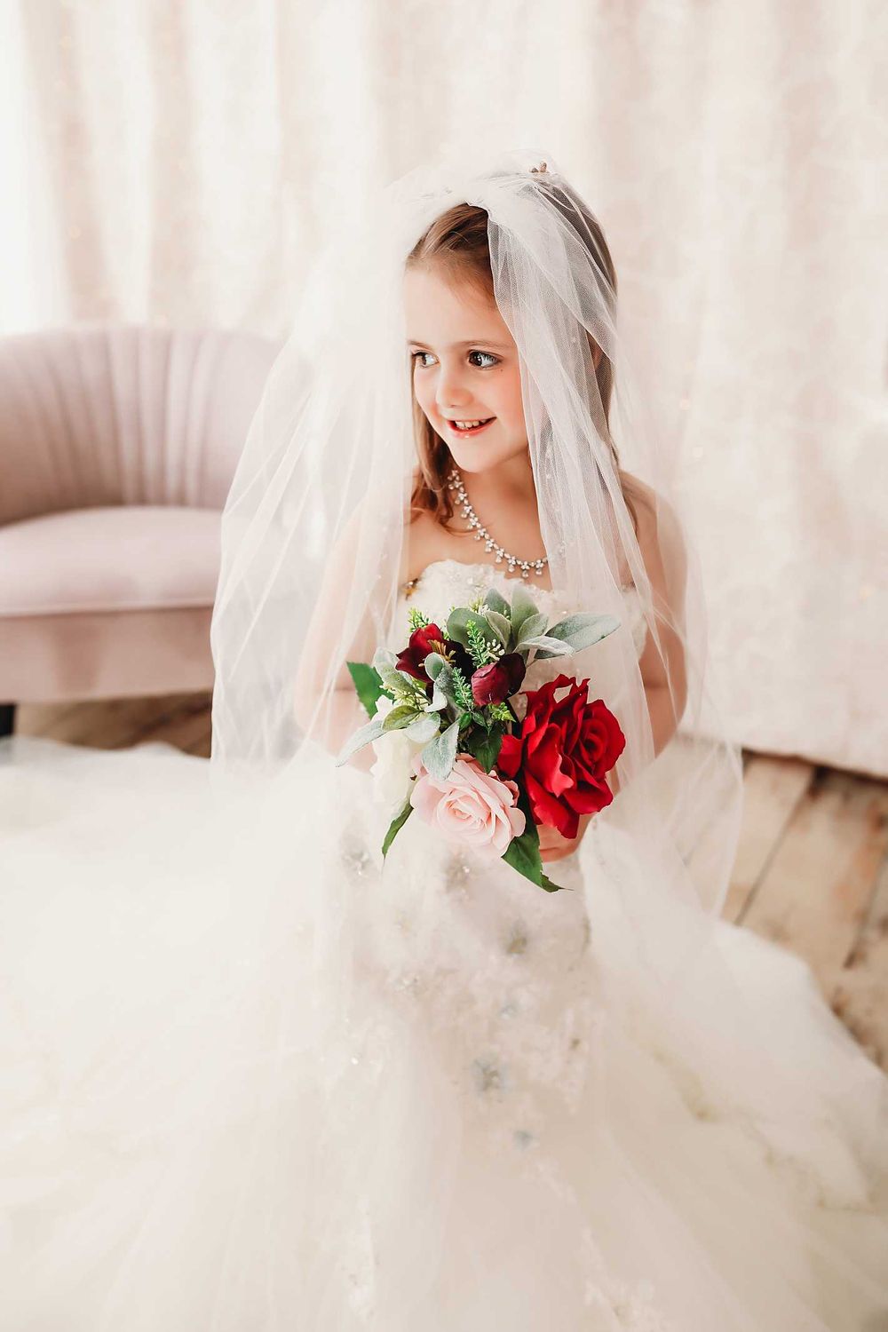 Portrait in white wedding dress with red and pink bouquet against light background.