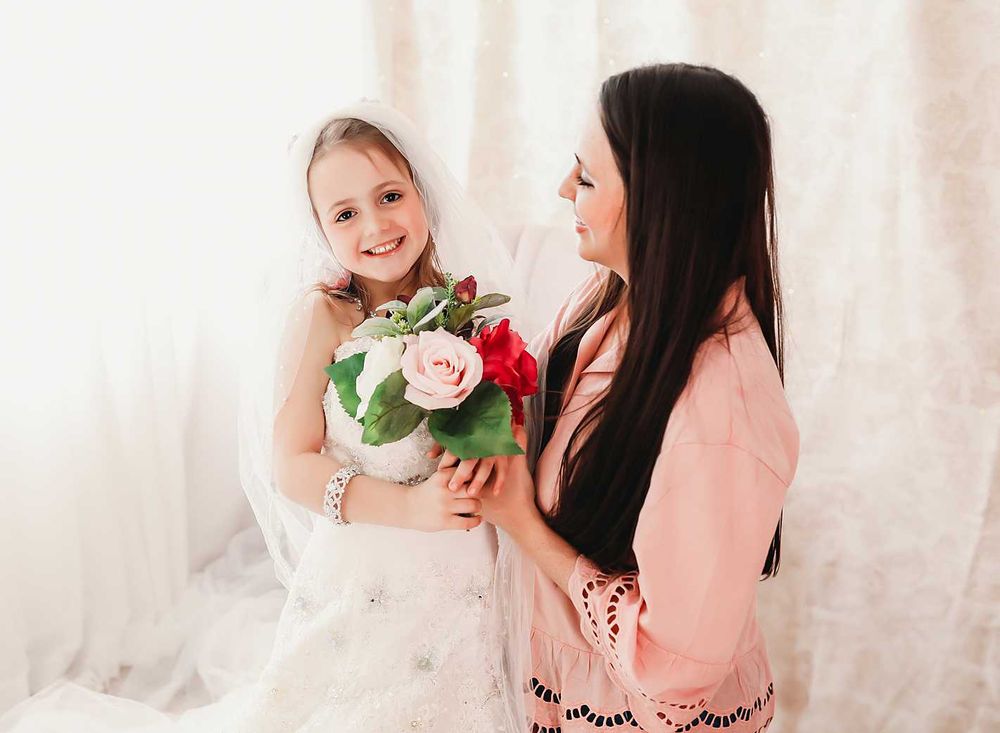 Elegant portrait with soft lighting and pink roses against white backdrop.
