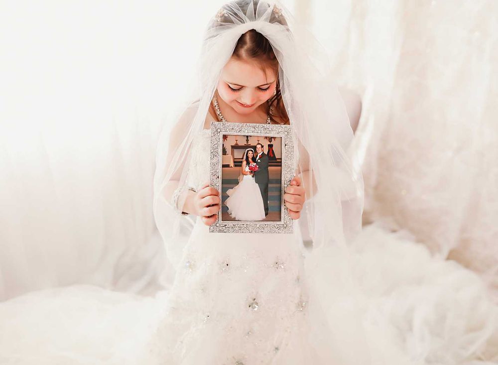 Portrait in white dress holding framed photograph against light backdrop.