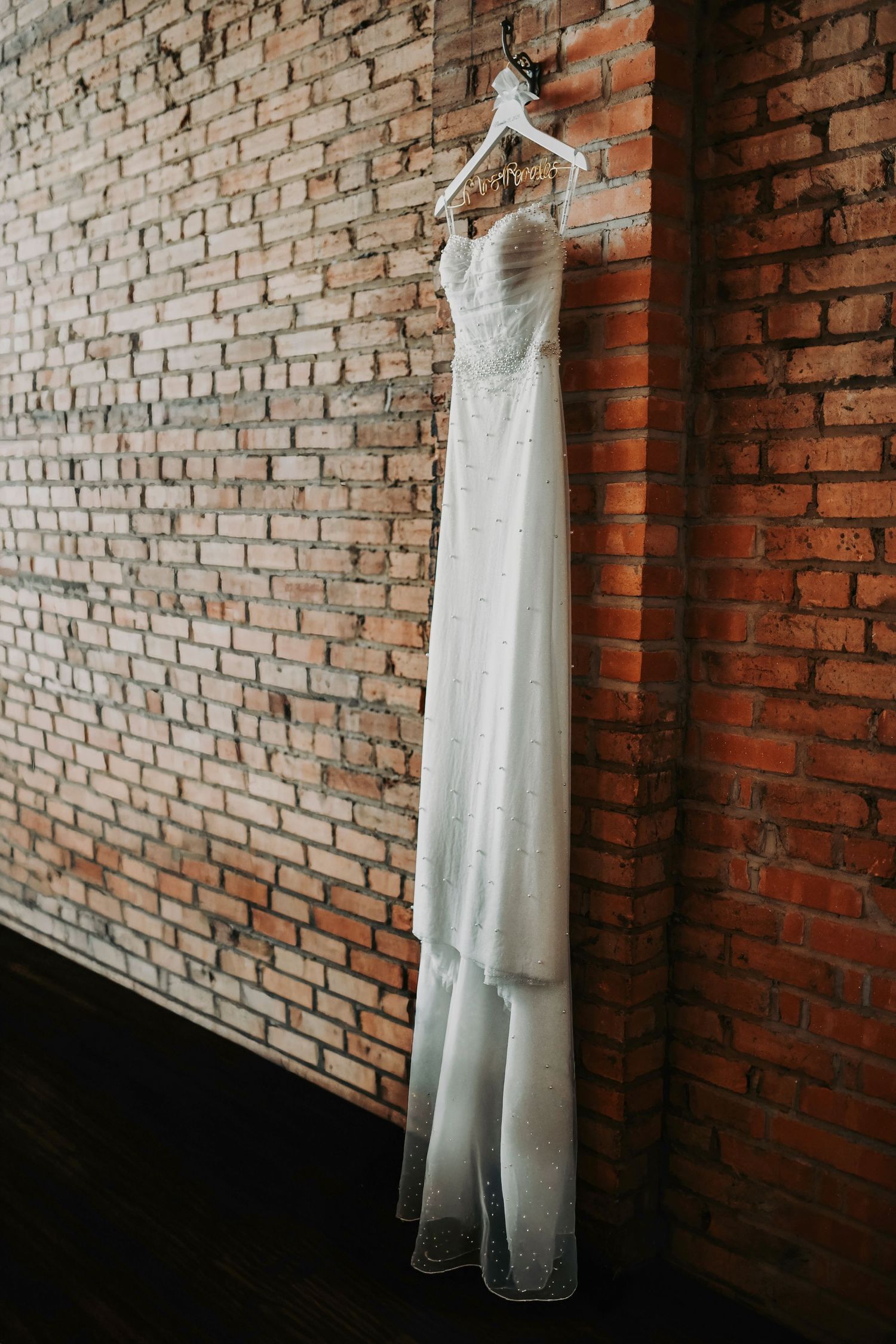 Modern wedding gown hanging against exposed brick inside Brake & Clutch Warehouse.