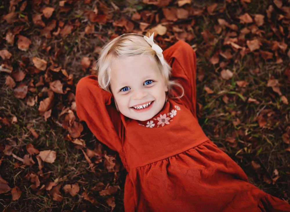 A series of connected photos showing someone in a bright red outfit lying on autumn leaves in a creative outdoor portrait sequence.