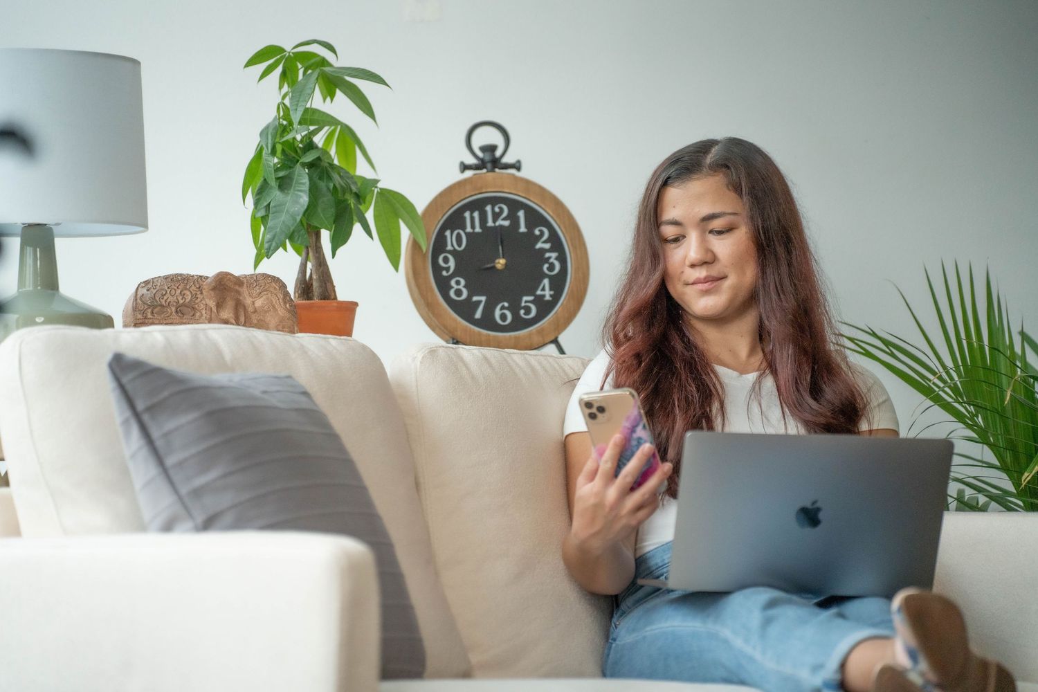 Cozy home office setup with laptop, plants, and wall clock in bright room.