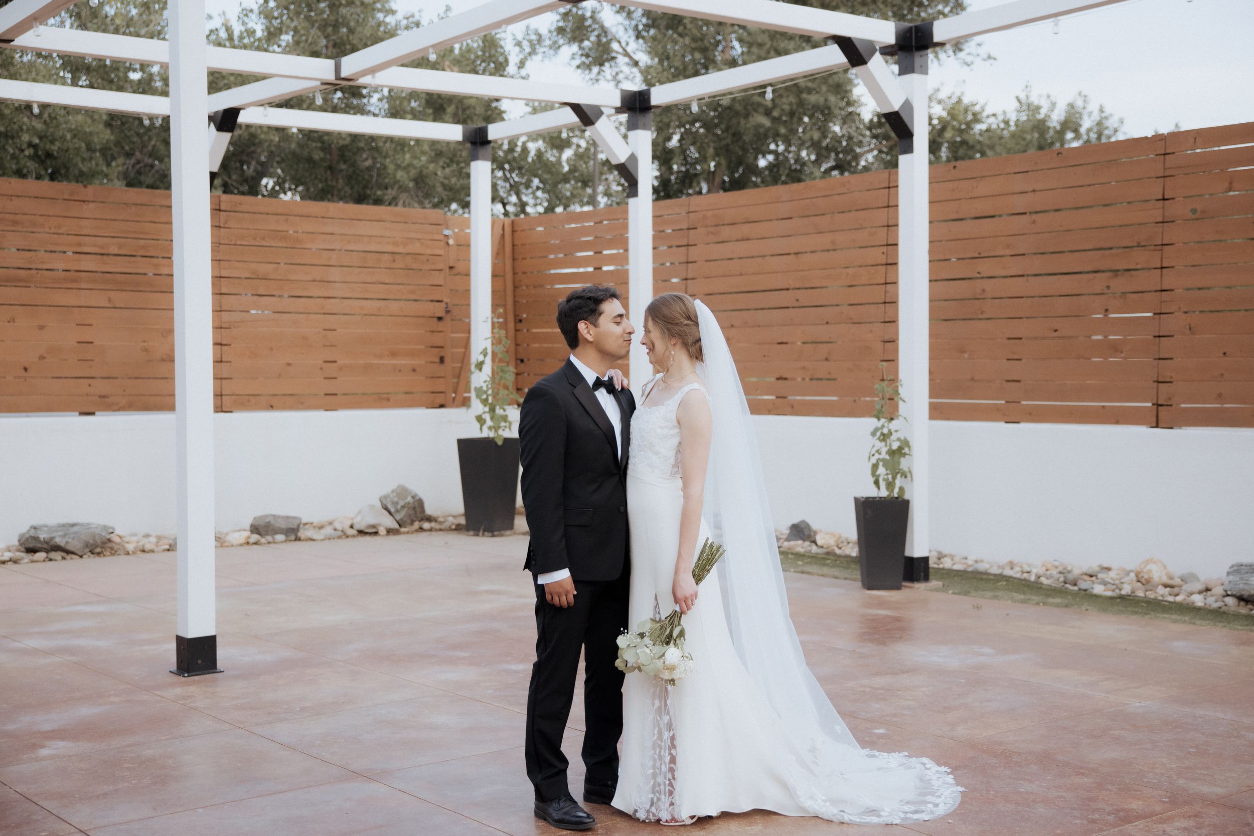 A couple shares a romantic moment under a white pergola during their outdoor wedding ceremony.