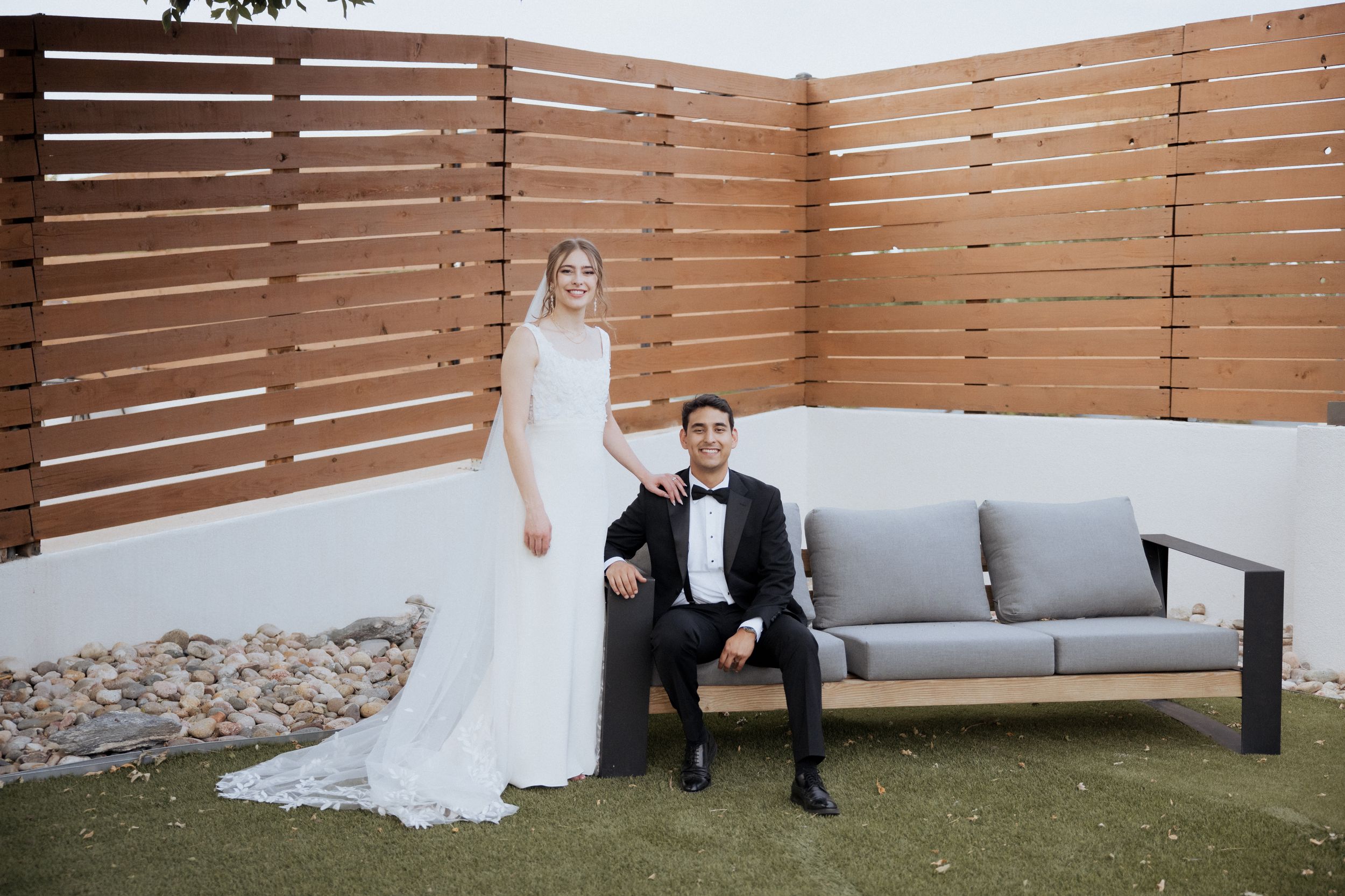 Wedding couple poses in front of modern wood slat wall during outdoor photo session.