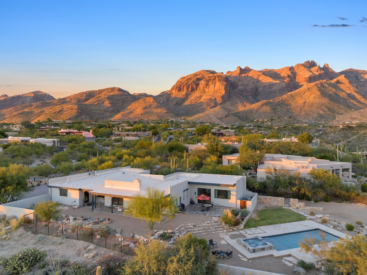 Desert mountain range glowing orange at sunset with residential buildings in the foreground.