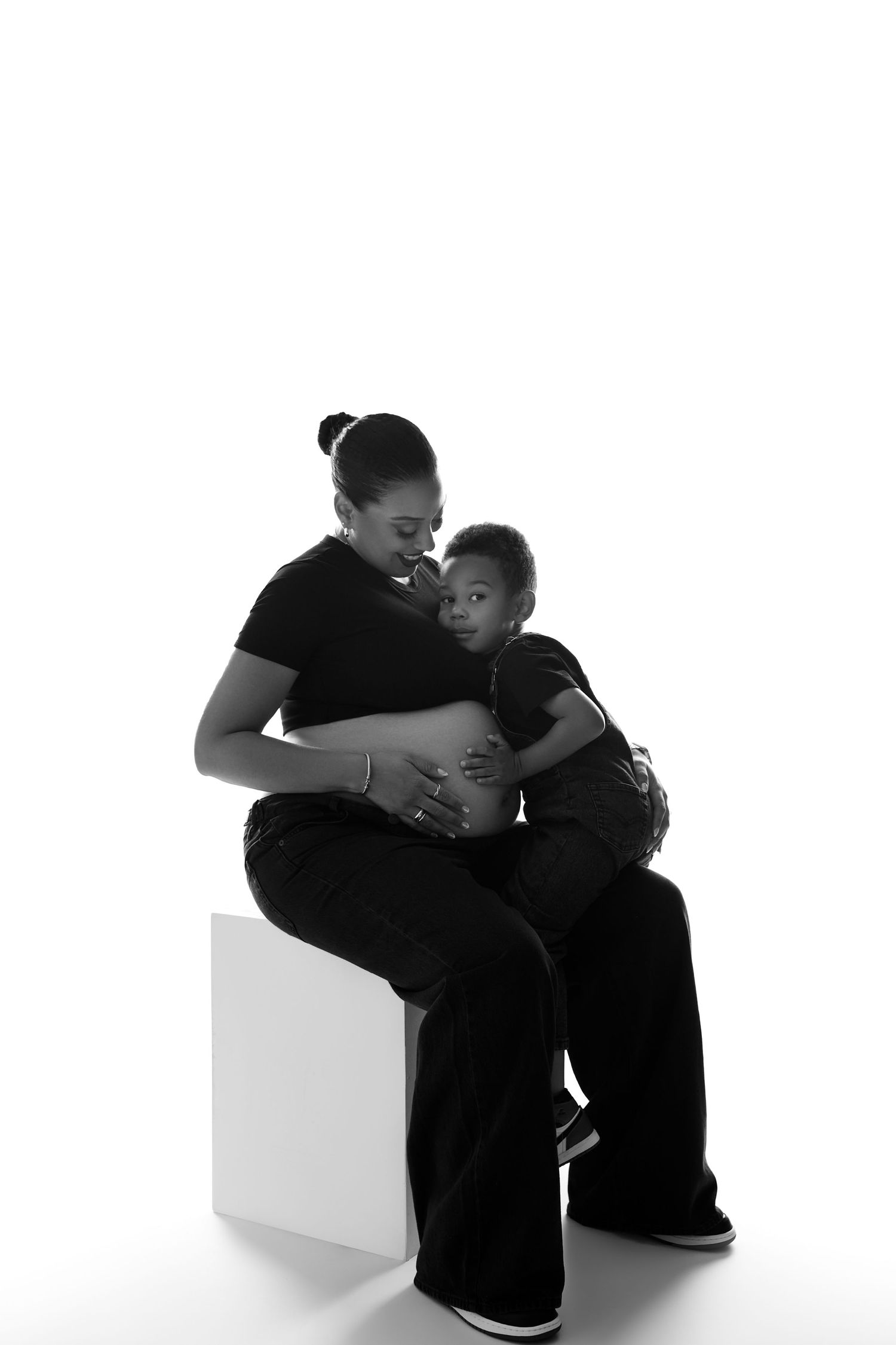 Two figures in black clothing share an intimate moment against a white background in a minimalist artistic composition.