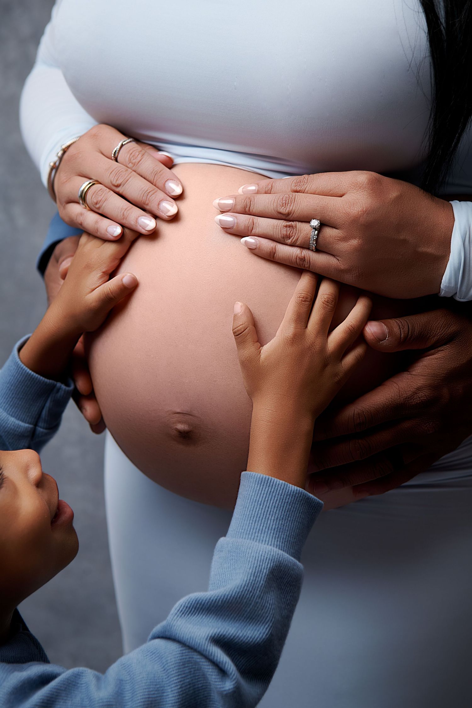 Close-up series showing hands gently touching and cradling a pregnant belly in white maternity clothing.