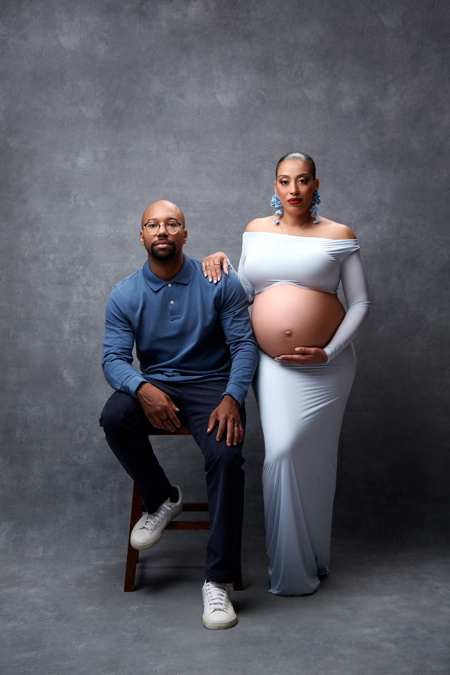 A series of maternity photos showing a couple in a studio with the pregnant person wearing a white dress and partner in blue.