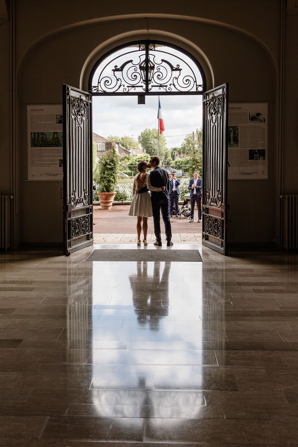 Reportage photo mariage Lille : maries s'embrassant a la sortie de la mairie de Lambersart dans l'entrebaillement de la porte