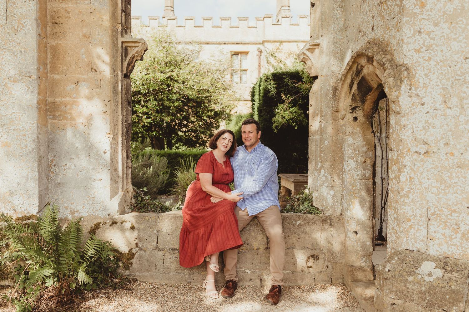 A couple in red and white outfits poses together in an elegant stone archway setting during a photo session.