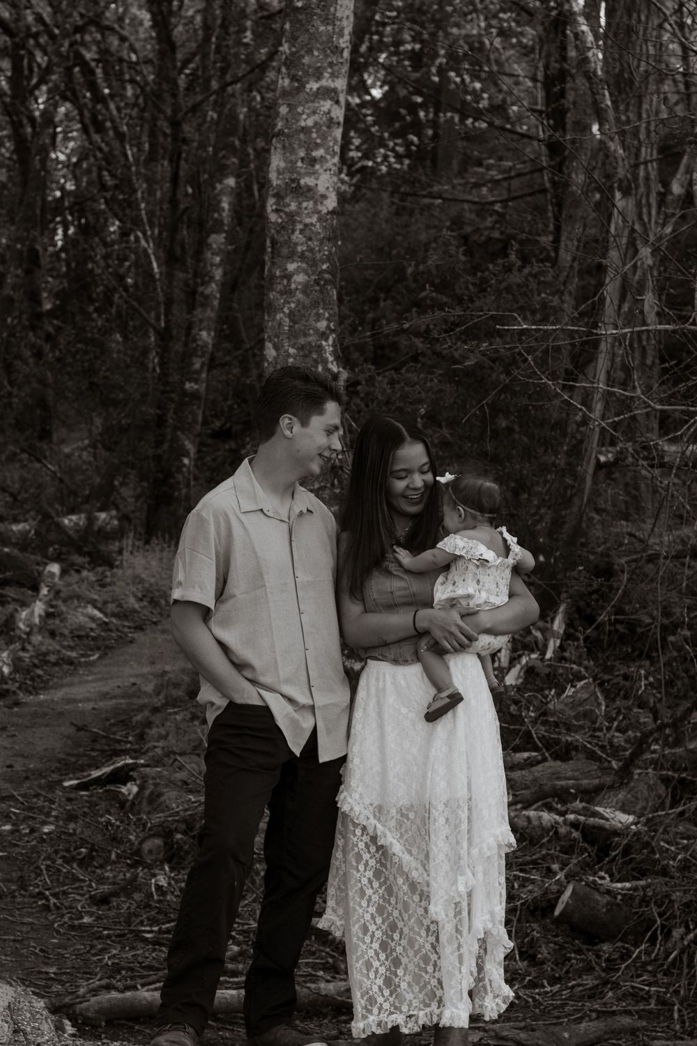 Black and white family portrait of couple with baby in a forest, woman in white lace dress holding baby at tolmie state park in olympia wa