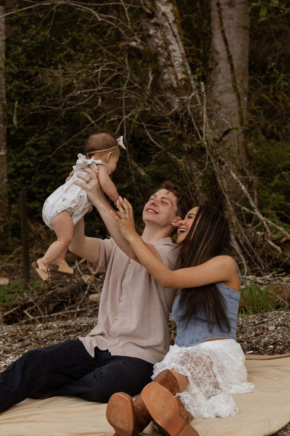 Happy young couple sitting outdoor lifting their baby girl in a forest setting at tolmie state park taken by olympia washington photographer