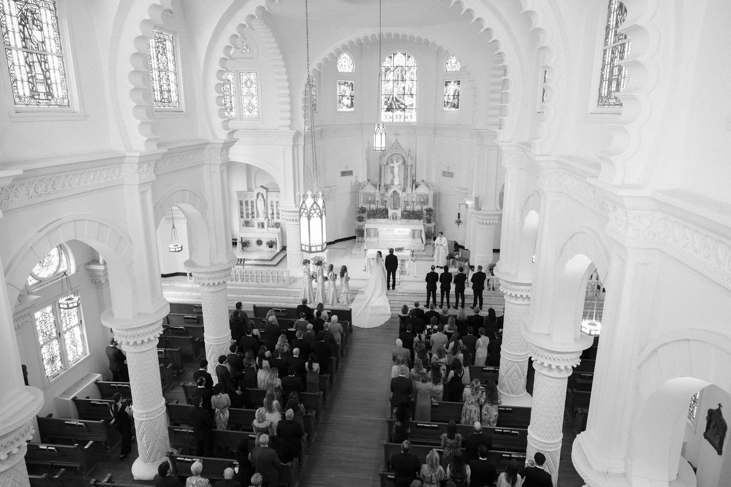 Black and white interior of a grand cathedral with vaulted arches and rows of pews filled with people.