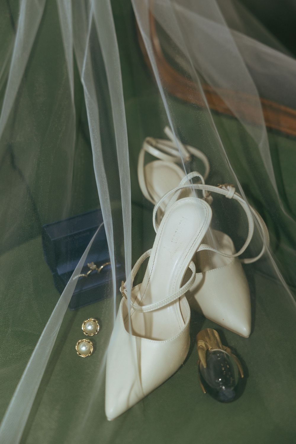 Elegant white bridal shoes with delicate straps and a small jeweled accent displayed against a soft green backdrop.
