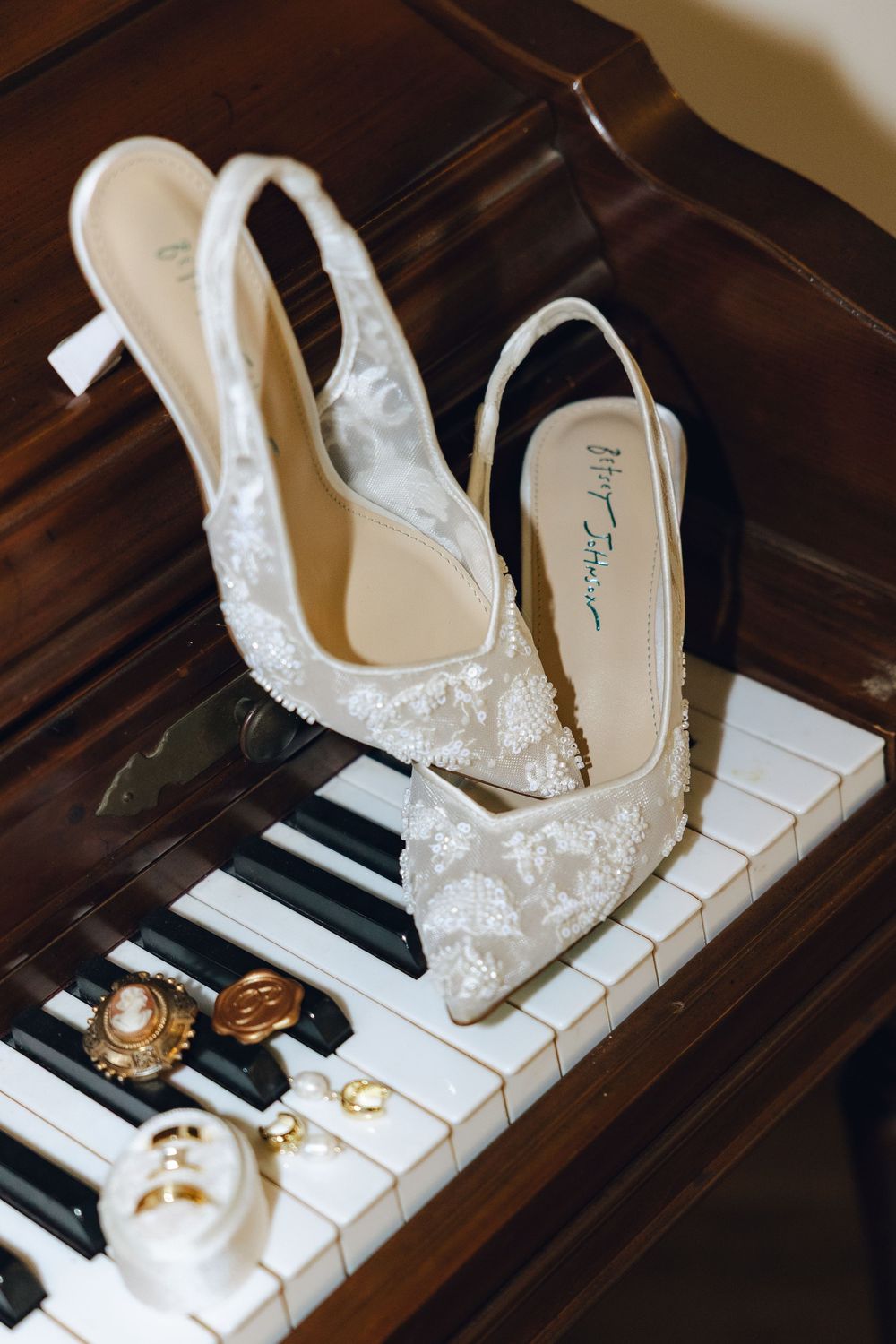 Elegant white lace bridal shoes displayed on piano keys with wedding rings create a romantic composition.