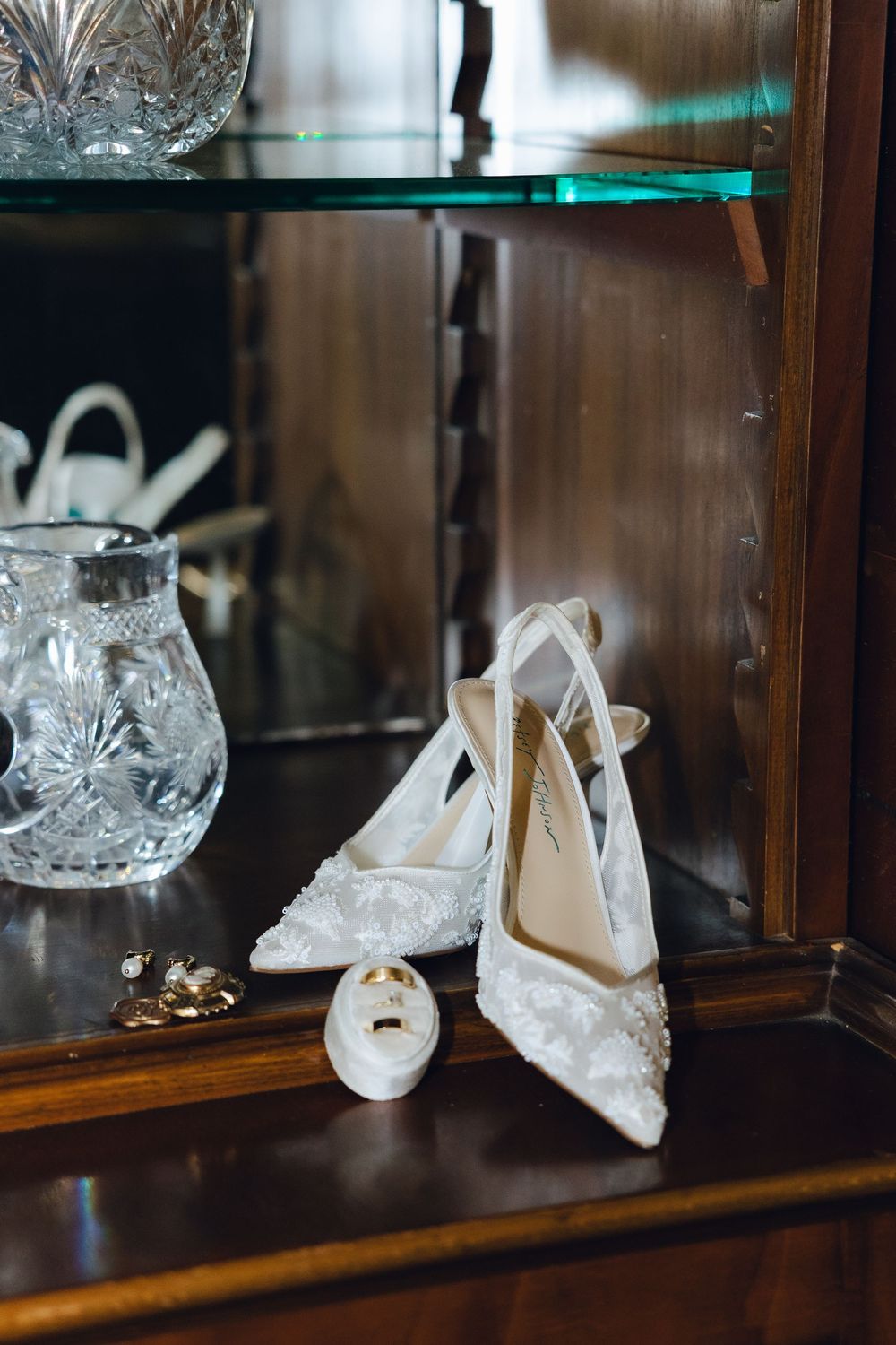 Elegant white bridal shoes displayed in glass cases with crystal decorative elements in a boutique setting.