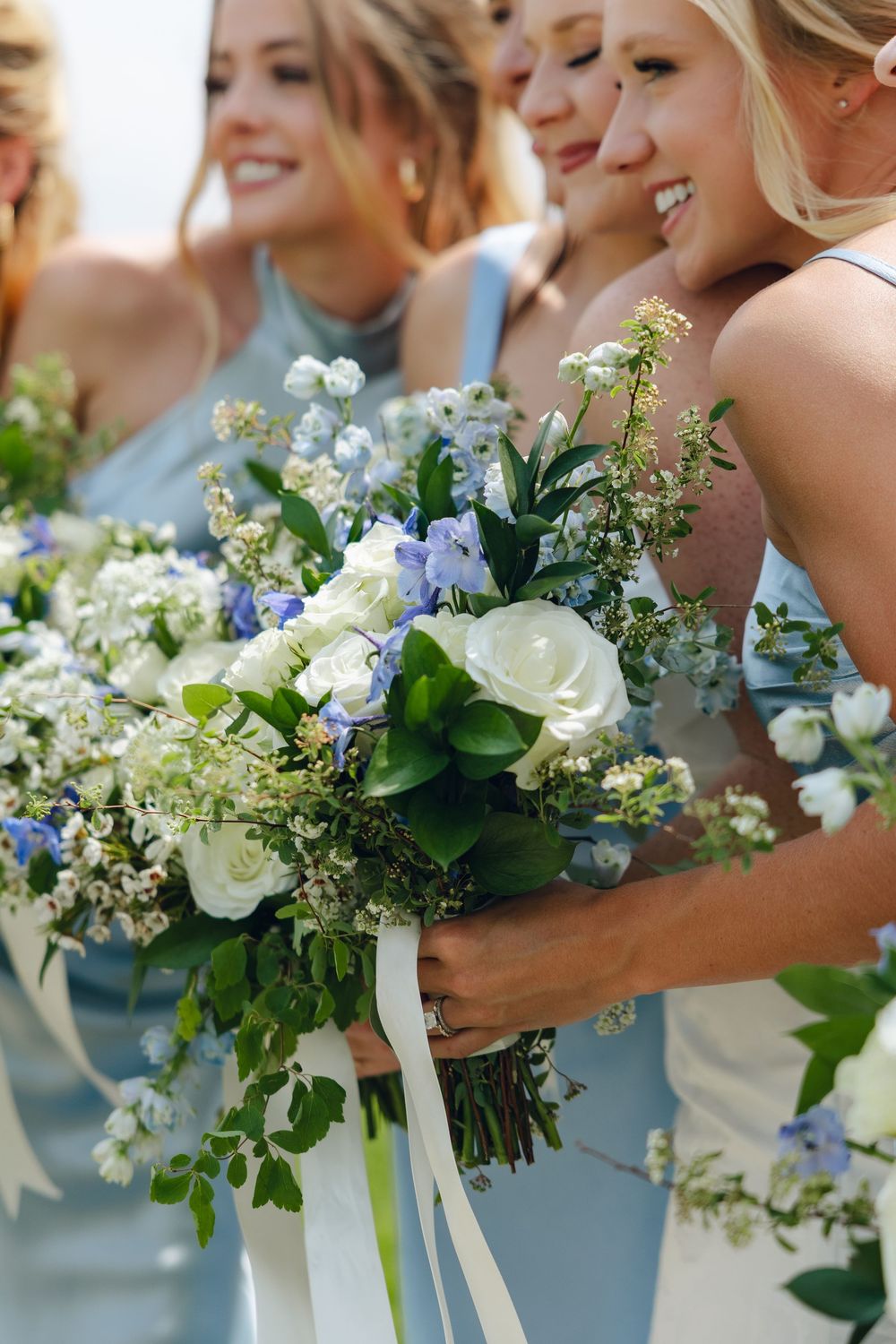 Row of bridesmaids holding elegant blue and white floral bouquets with delicate greenery at a wedding ceremony.