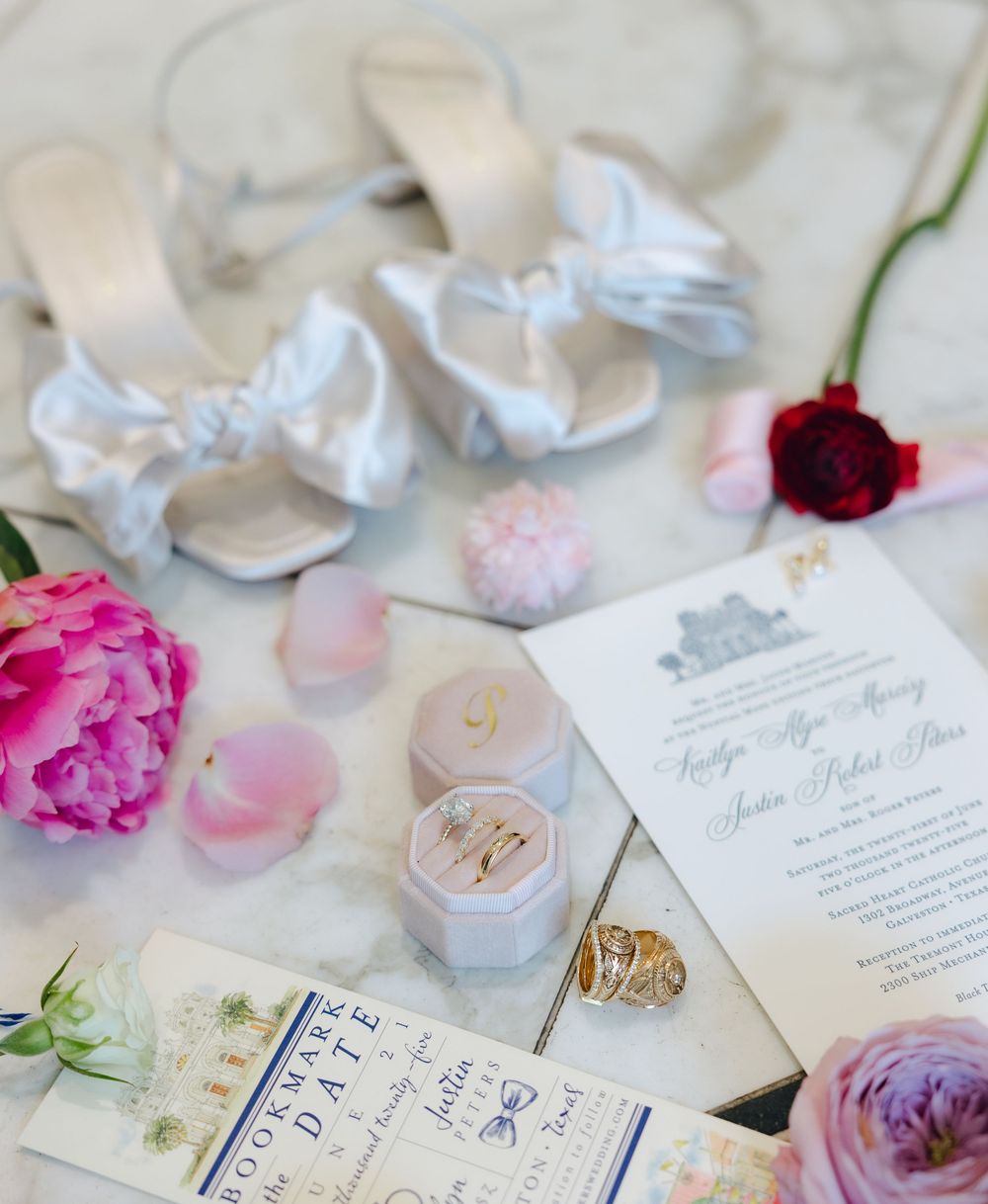 Elegant wedding invitation suite with white and pink rose petals scattered around delicate calligraphy and ring details.