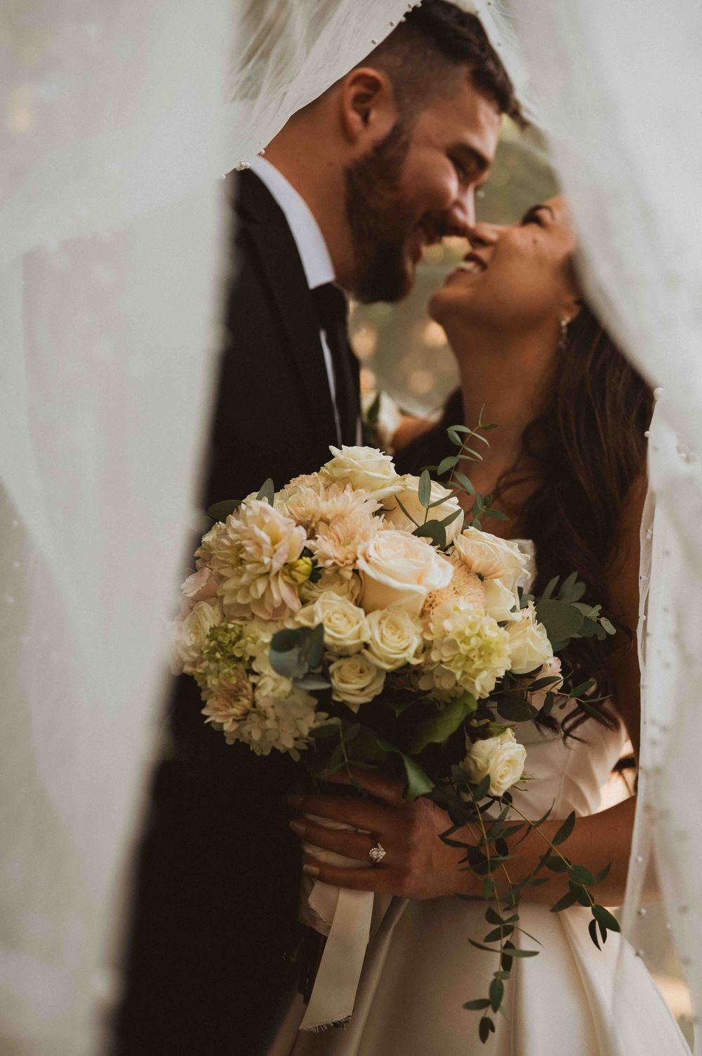 Romantic wedding couple shares intimate moments in soft lighting with elegant white rose and hydrangea bouquet.