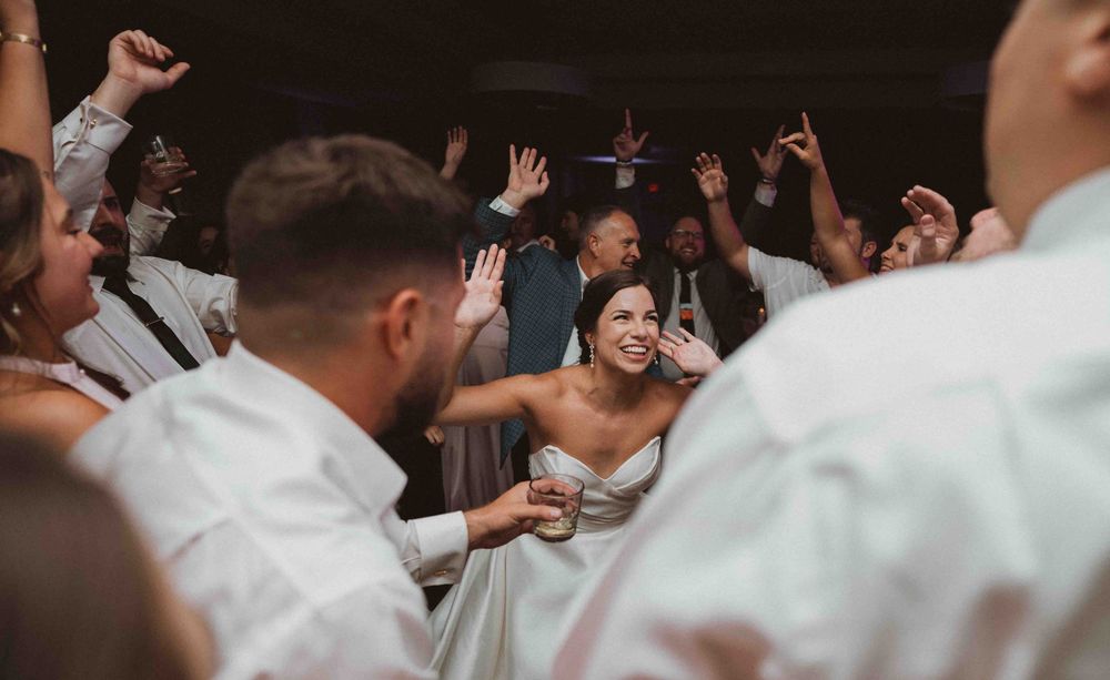 A group of people wearing white clothing dance and celebrate together at an indoor event.