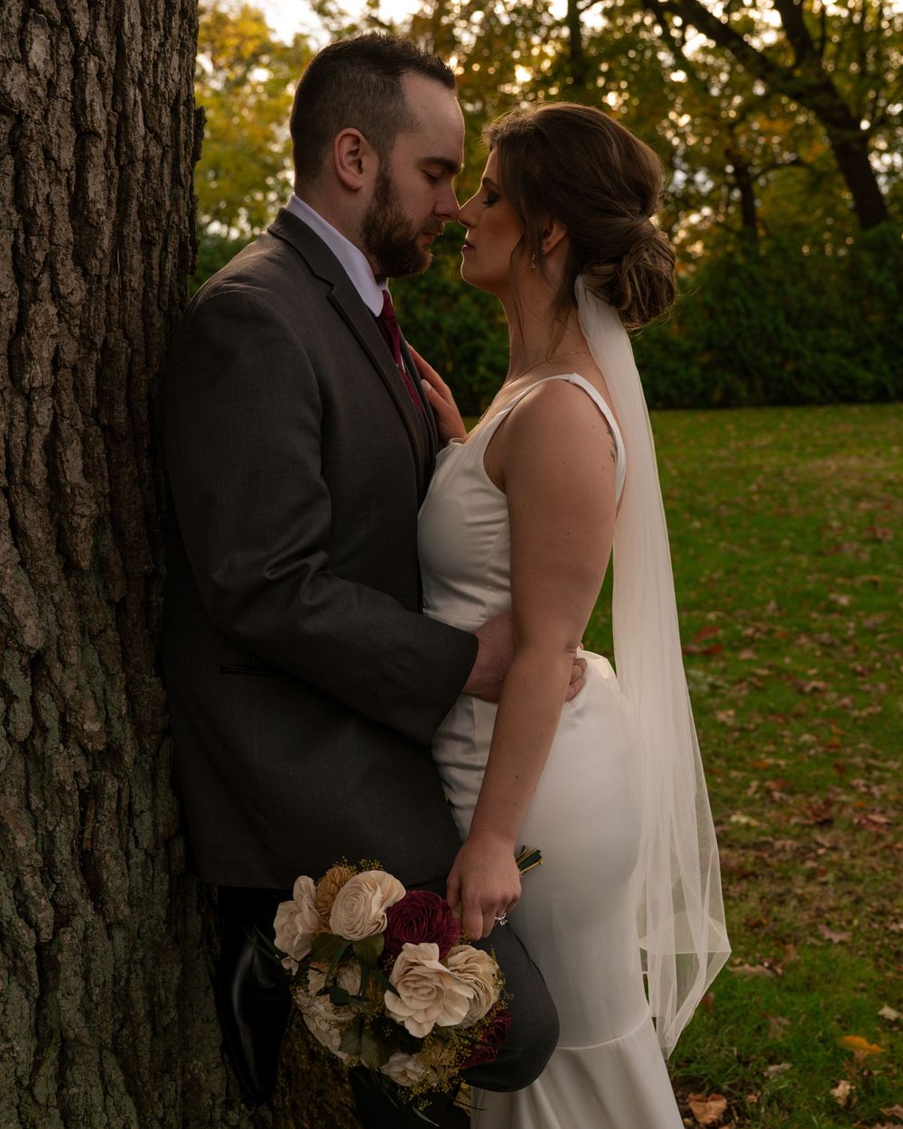 A romantic wedding couple shares intimate moments in a wooded outdoor setting during golden hour.