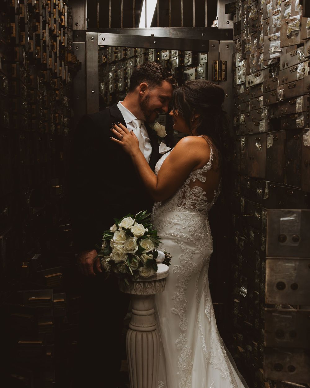 A couple shares an intimate moment in front of a rustic brick wall during their wedding celebration.