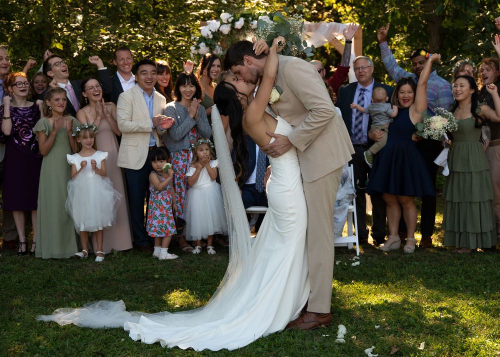 Wedding couple shares a romantic dip kiss during outdoor garden ceremony as guests look on and celebrate.