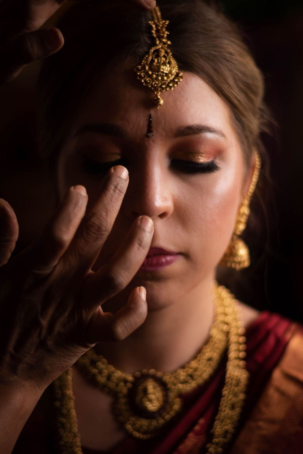 Artistic close-up portrait showing traditional Indian bridal jewelry and makeup against dark background.
