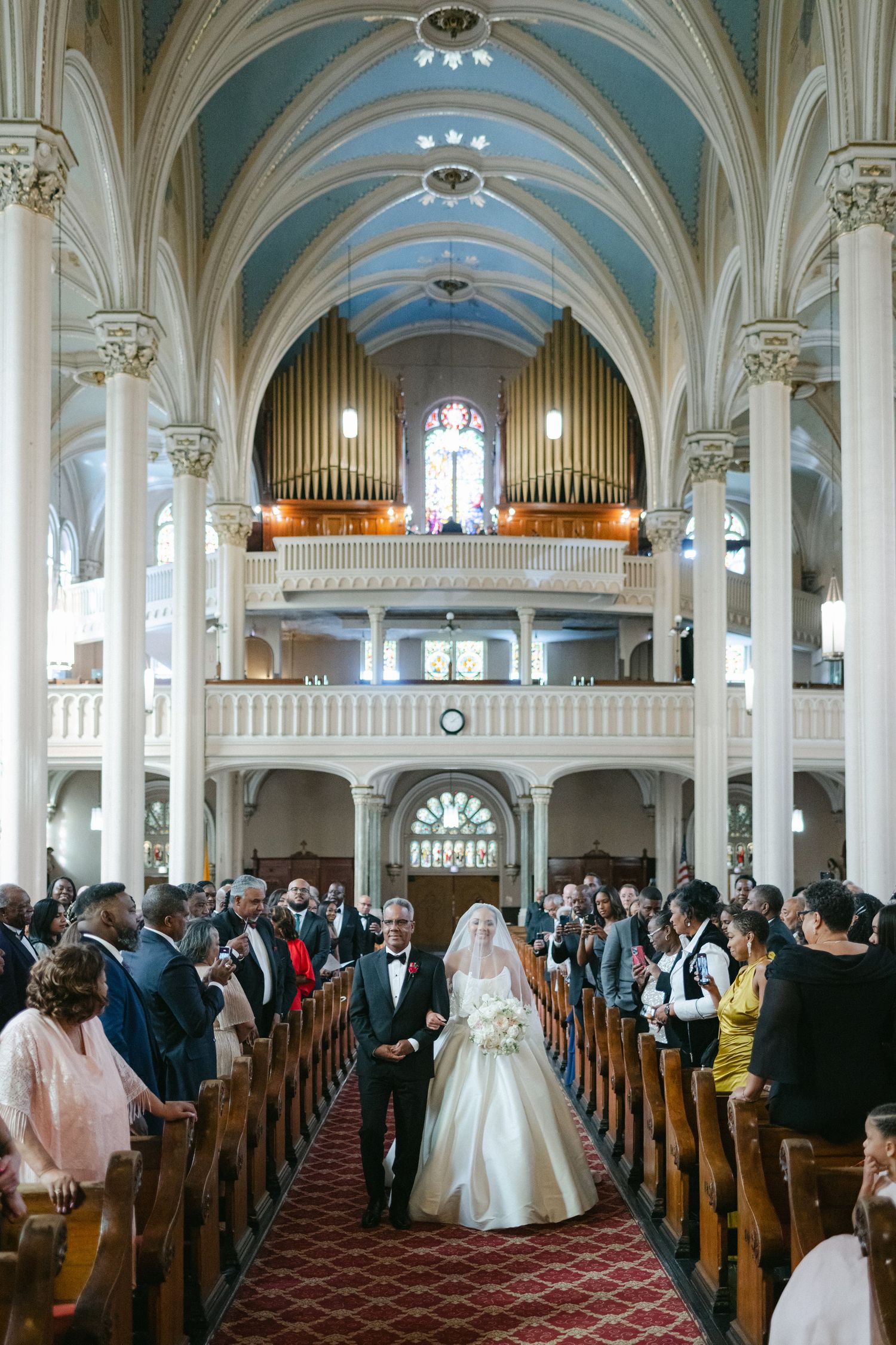 Panoramic view of a church wedding ceremony with ornate architecture, arched ceilings, and organ pipes at the altar.