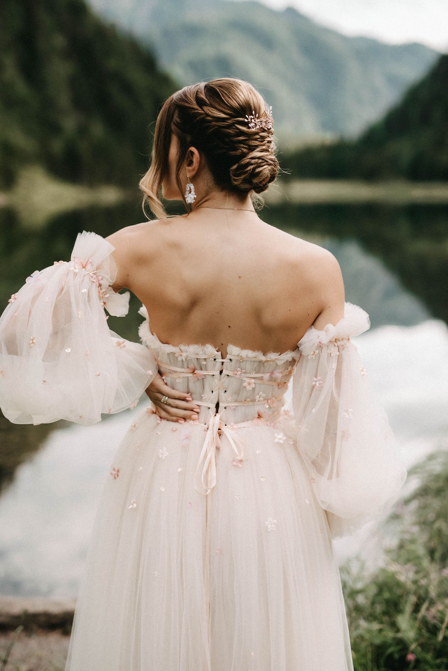 Ethereal off-shoulder wedding dress with delicate details photographed against mountain landscape.