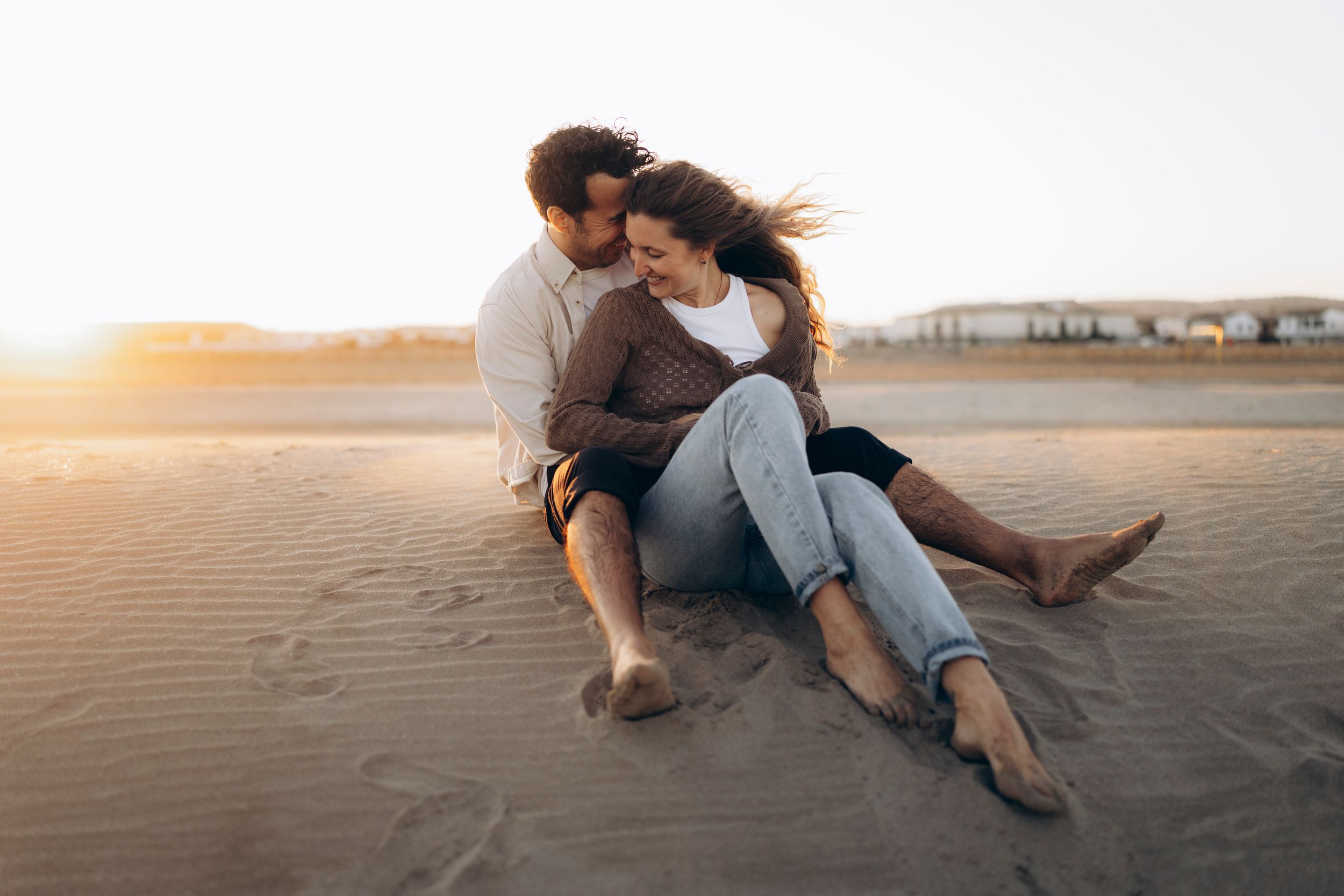 A romantic couple embraces on a dirt path at golden hour with trees silhouetted in the background.