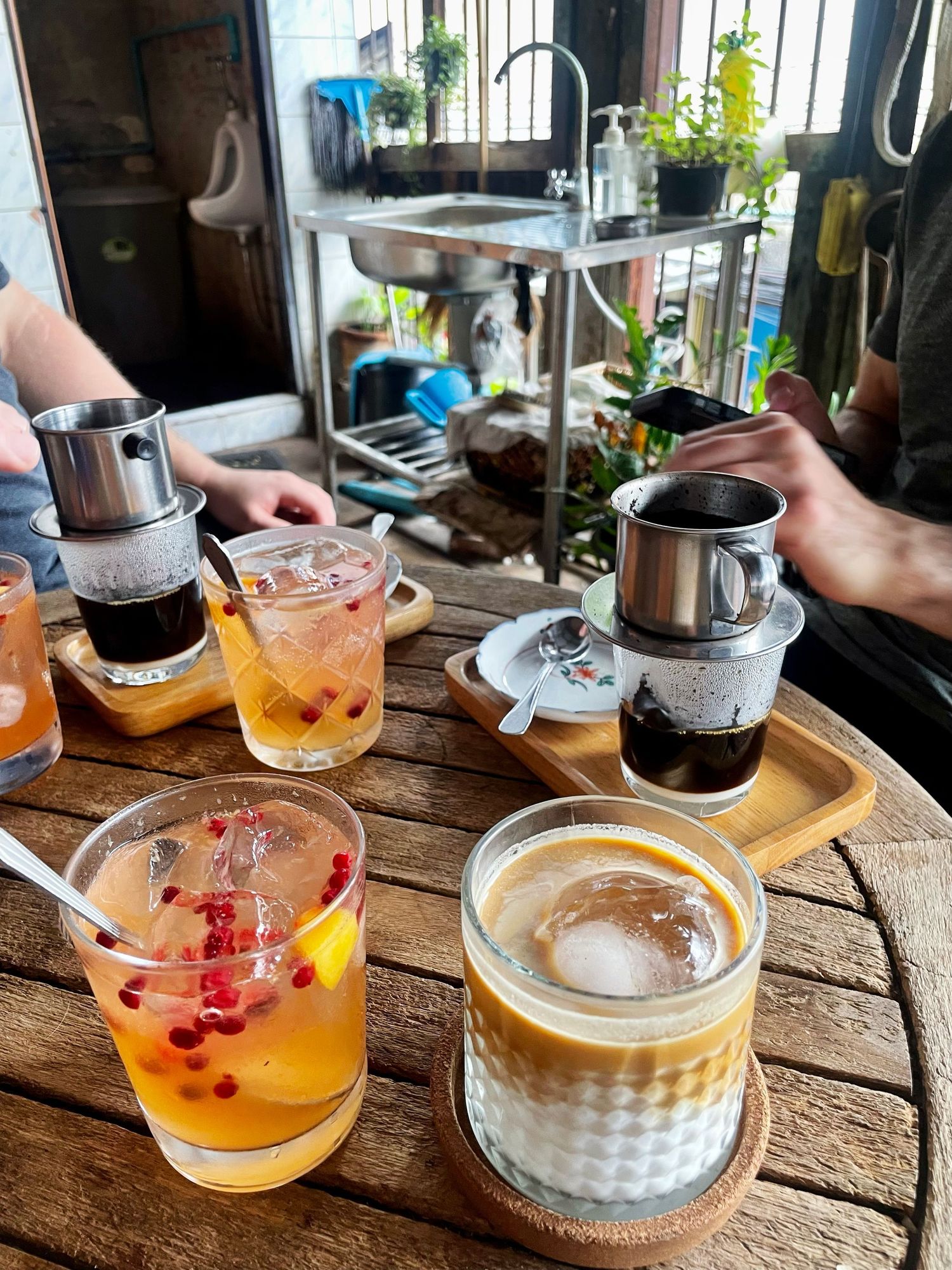 Tea service on rustic wooden table shows multiple glass teapots with fruit-infused beverages and honey-colored drinks.