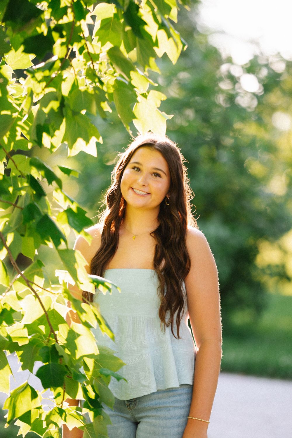 A portrait photoshoot in a park with sunlit trees and leaves creating a natural green backdrop.
