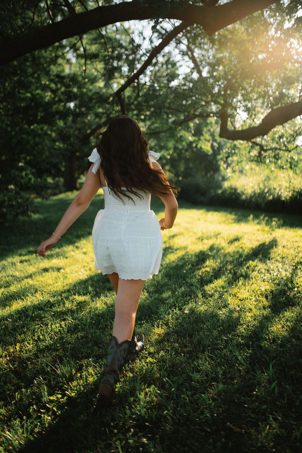Person in white dress twirling through a sunlit meadow at golden hour with long shadows on green grass.