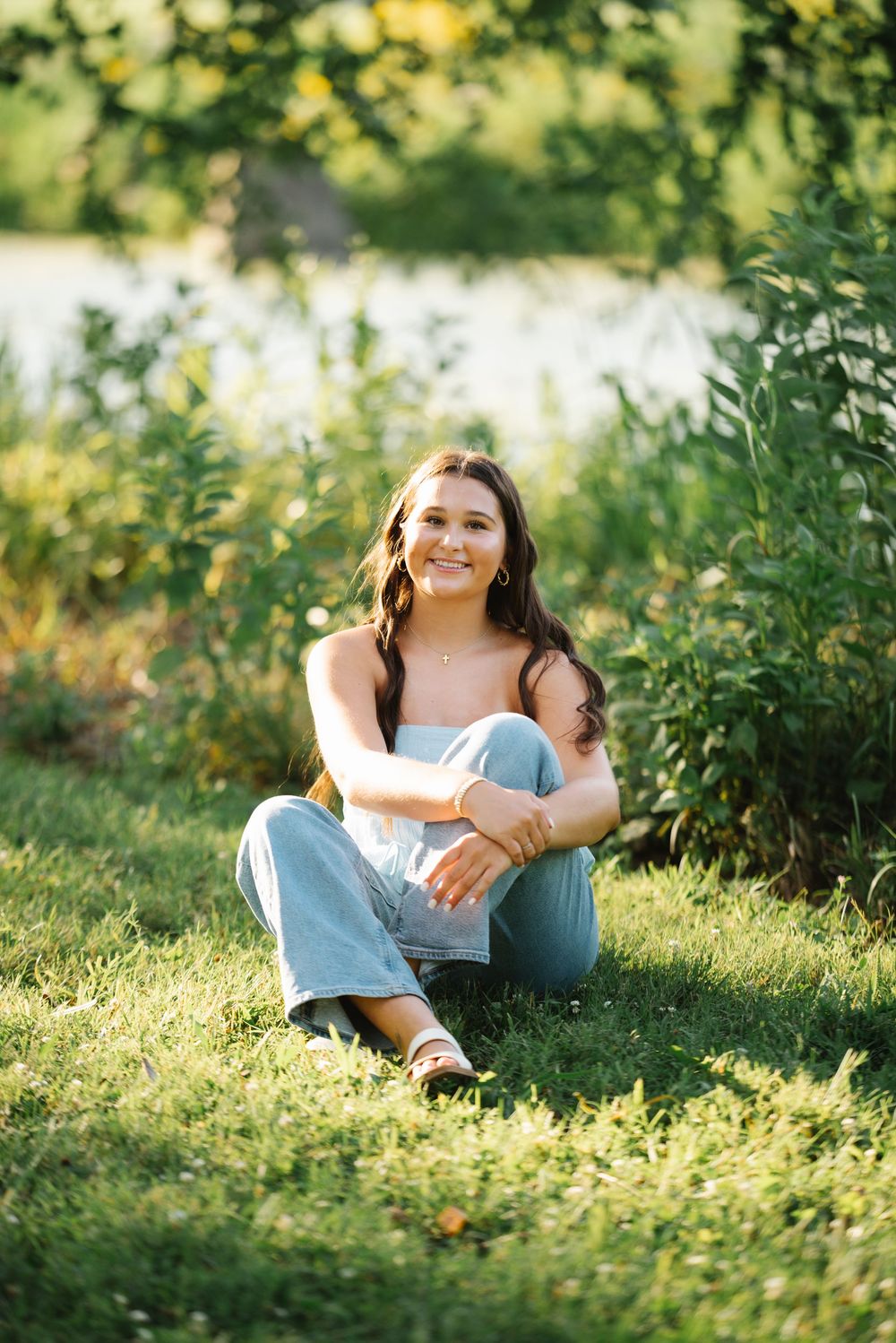 A person sits on green grass in a sunny outdoor setting, surrounded by lush foliage and natural lighting.
