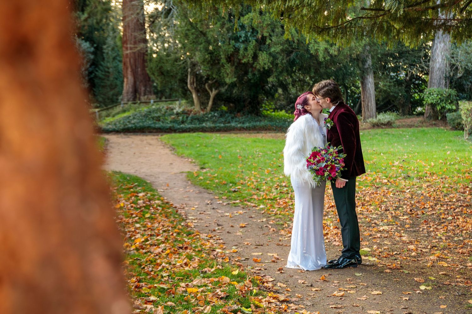Wedding party walking along tree-lined autumn path with fallen leaves.