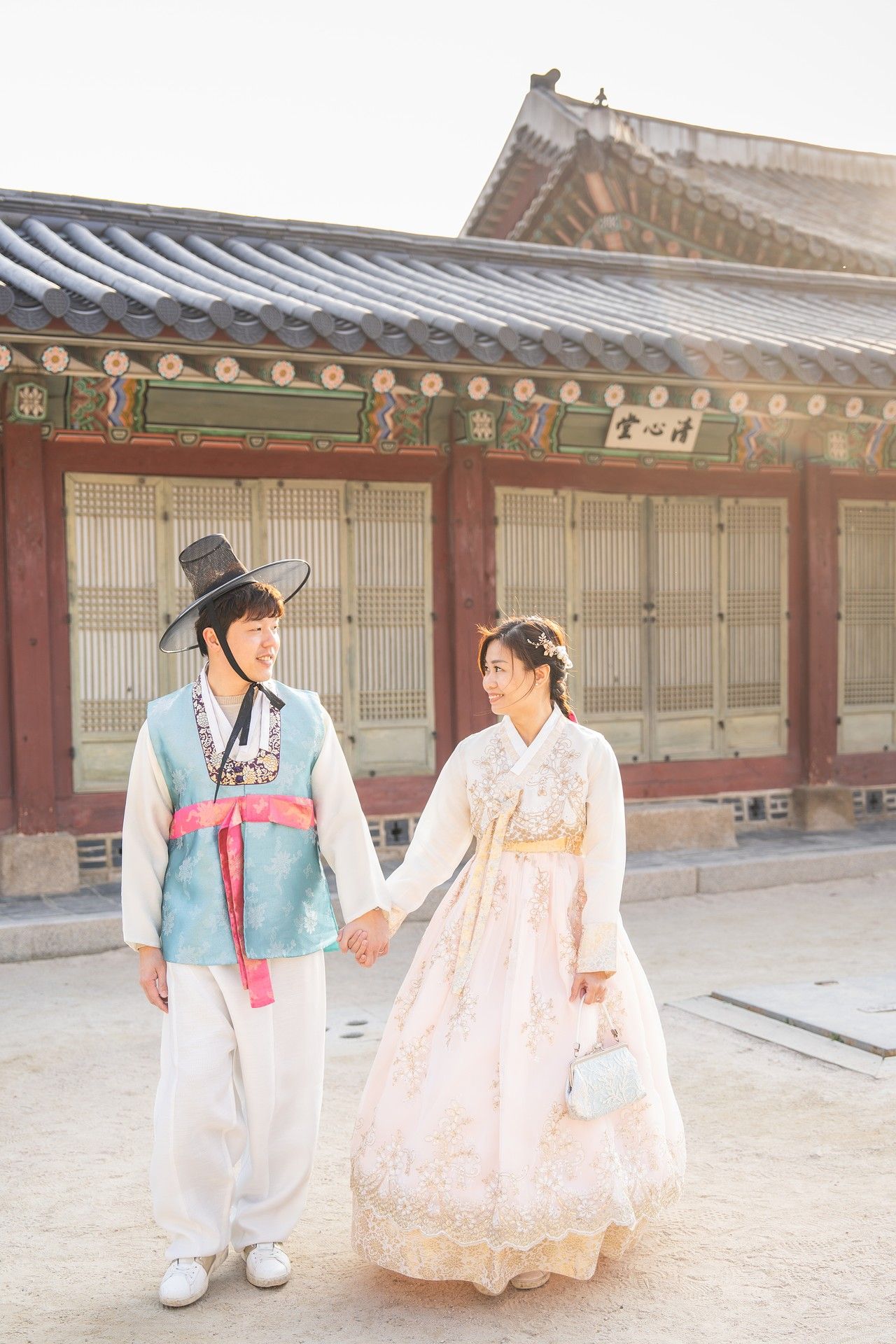 A couple in traditional Korean hanbok attire poses together in a historic palace courtyard setting.